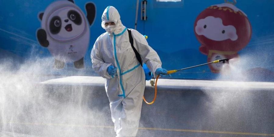 Ein Arbeiter versprüht Desinfektionsmittel vor einem Hotel in Peking. Foto: Natacha Pisarenko/AP/dpa