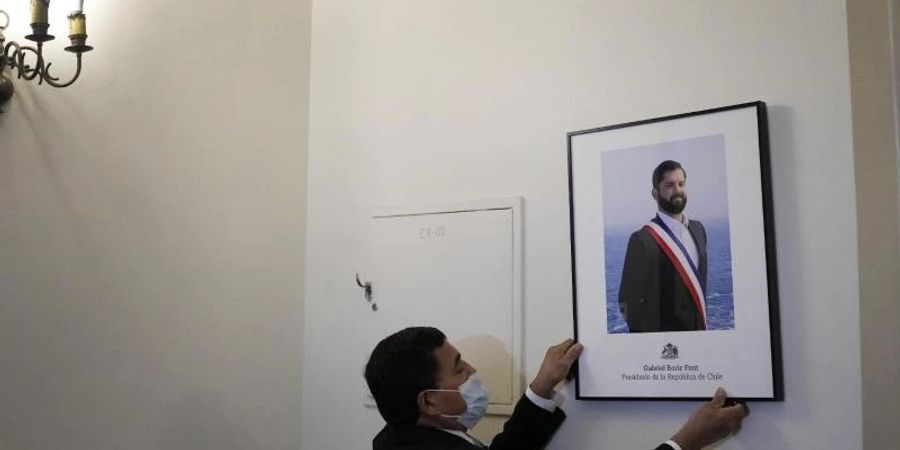 Ein Palastangestellter hängt das offizielle Porträt des neuen chilenischen Präsidenten Boric im Büro des Präsidentenpalastes La Moneda auf. Foto: Matias Delacroix/AP/dpa