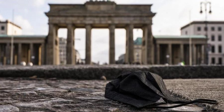 Eine schwarze Corona-Makse liegt auf dem Boden vor dem Brandenburger Tor. Foto: Christophe Gateau/dpa