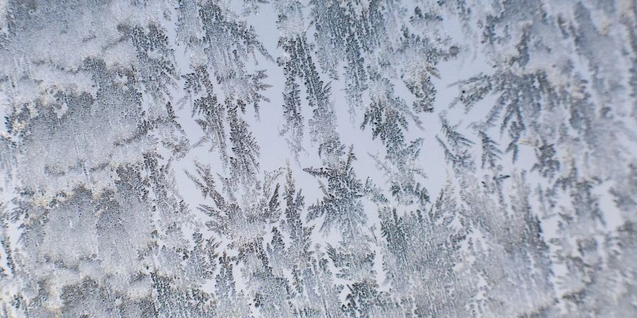 Eiskristalle zeichnen auf einer Autoscheibe ab.