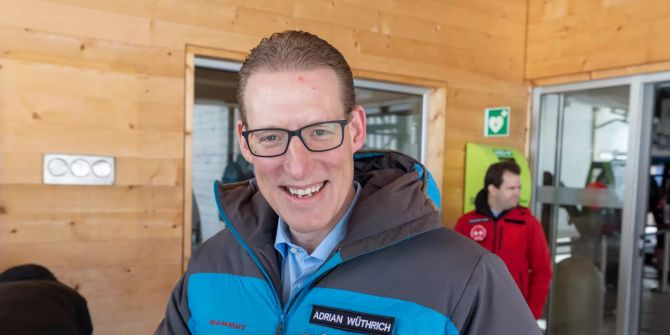 Mann mit Brille und kurzen Haaren in Winterjacke vor Holzhütte