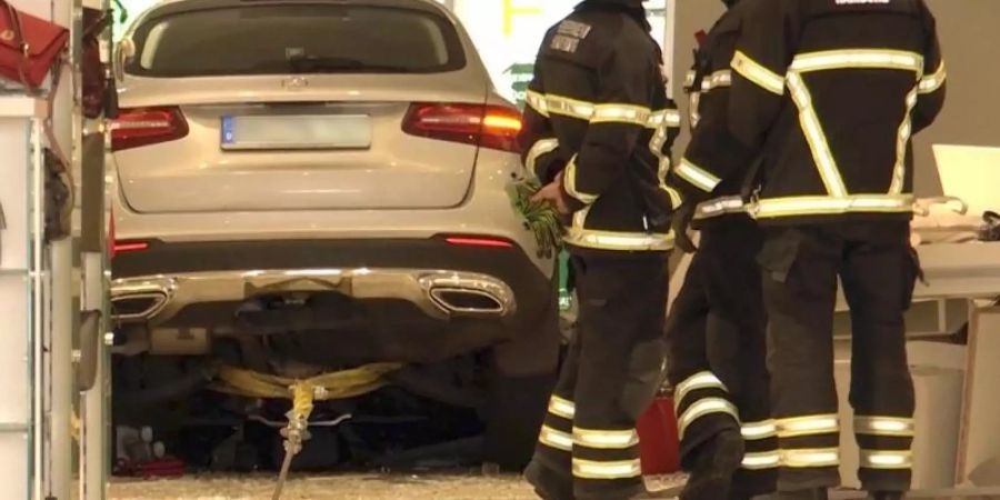 Feuerwehrleute stehen neben einem Auto, das in ein Kaufhaus gefahren ist. Der etwa 75 Jahre alte Fahrer sei leicht verletzt worden. Foto: TNN