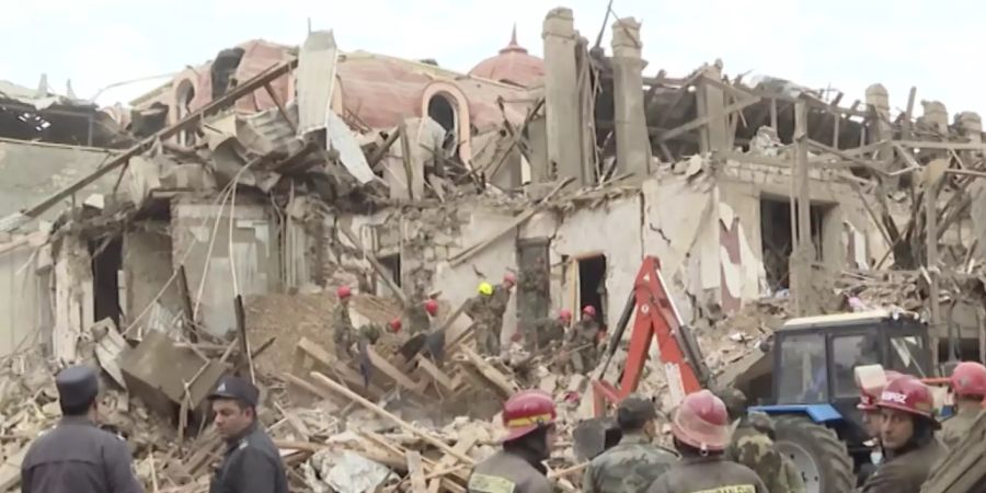 Rettungssanitäter und Zivilisten stehen vor den Trümmern eines zerstörten Gebäudes, nachdem die Stadt während der Kämpfe um das separatistische Gebiet Berg-Karabach von armenischer Artillerie beschossen wurde (Ausschnitt aus einem Video). Mehrere Zivilisten wurden getötet und Dutzende verwundet. Foto: Uncredited/AP/dpa