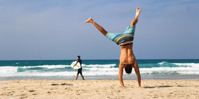Ein Mann in Badehose macht am Strand einen Handstand. Handstand Strand