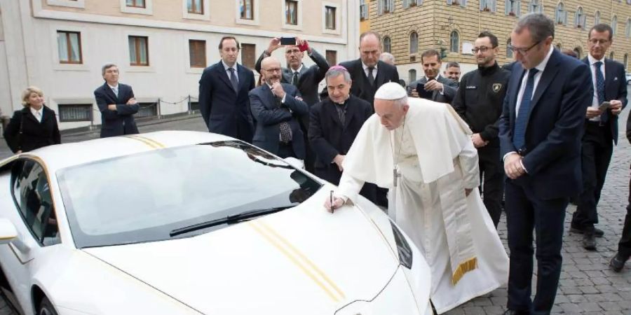 Papst Franziskus signiert den weissen Lamborghini, der ihm vom italienischen Sportwagenhersteller geschenkt wurde. Foto: L'Osservatore Romano/AP