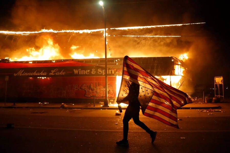 Ein Demonstrant trägt neben einem brennenden Gebäude eine US-Flagge während der Proteste.