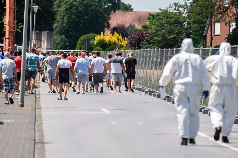 Bewohner der abgesperrten Siedlung in Sürenheide gehen zurück zu ihren Wohnhäusern, gefolgt von Bundeswehrsoldaten in Schutzanzügen.