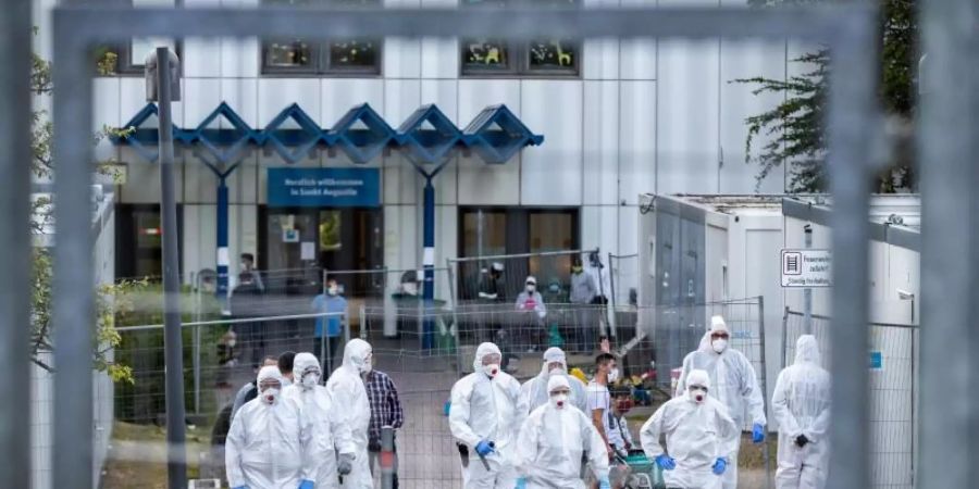 Beamte der Polizei und des Ordnungsamtes in Schutzanzügen vor der St. Augustiner Flüchtlingsunterkunft in NRW. Foto: Marcel Kusch/dpa