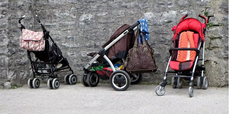 Drei Kinderwagen stehen an einer Wand.