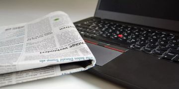 Eine Zeitung und ein Laptop sind auf einem Tisch.