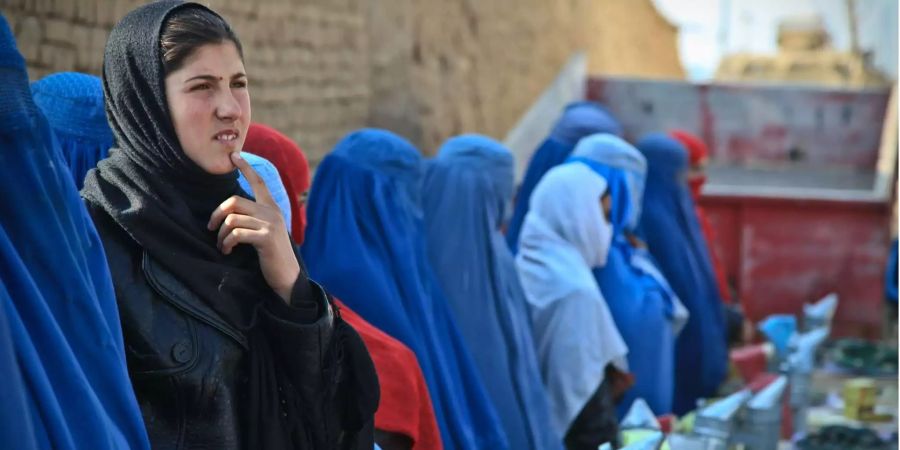 Eine muslimische Frau steht nachdenklich auf einem Markt und blickt in die Ferne.