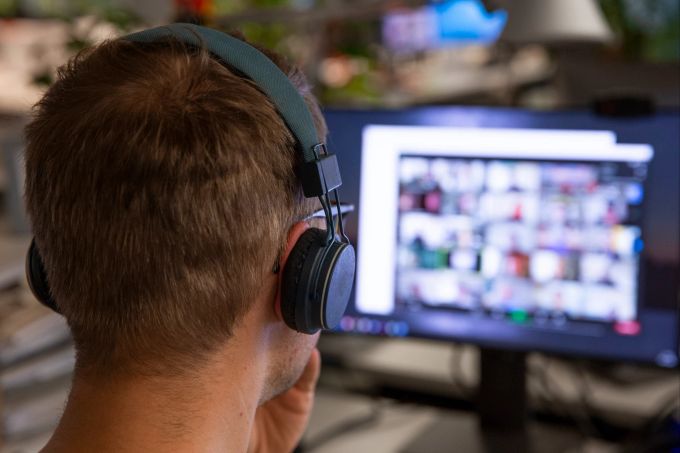 Ständig sich und andere beobachten: einer der Gründe, warum wir lange Online-Meetings so anstrengend finden. Mann Kopfhörer Computer Bildschirm