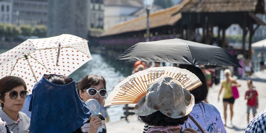 Touristen aus Asien trotzen der Hitze vor der Kapellbruecke in der Stadt Luzern am Dienstag, 22. August 2023. (KEYSTONE/Urs Flueeler).