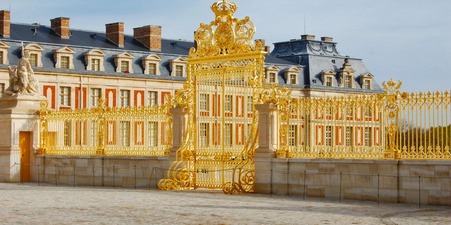 Das Goldene Tor, dahinter das Schloss von Versaille mit teilweise roter Fassade.