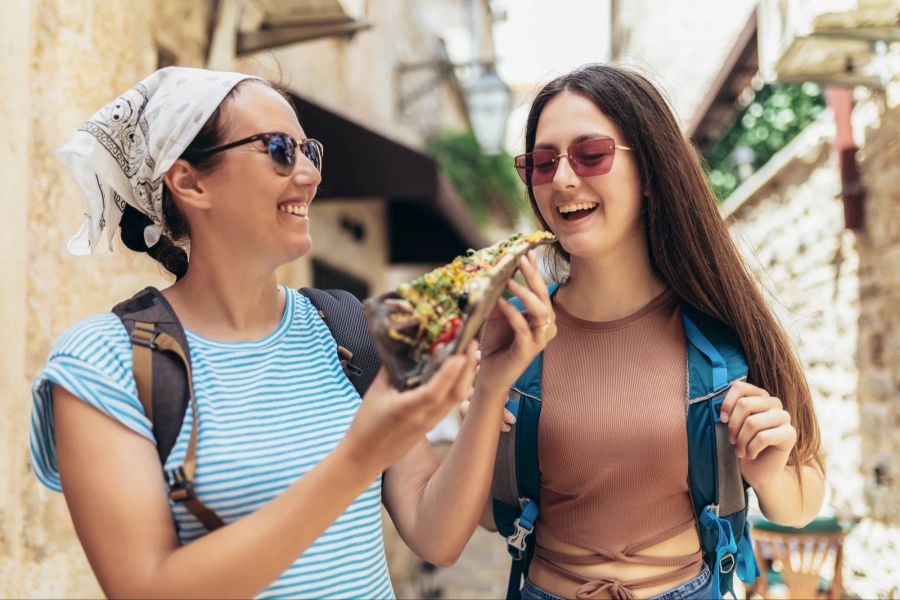 Zwei glückliche Frauen mit Rucksack essen Pizza