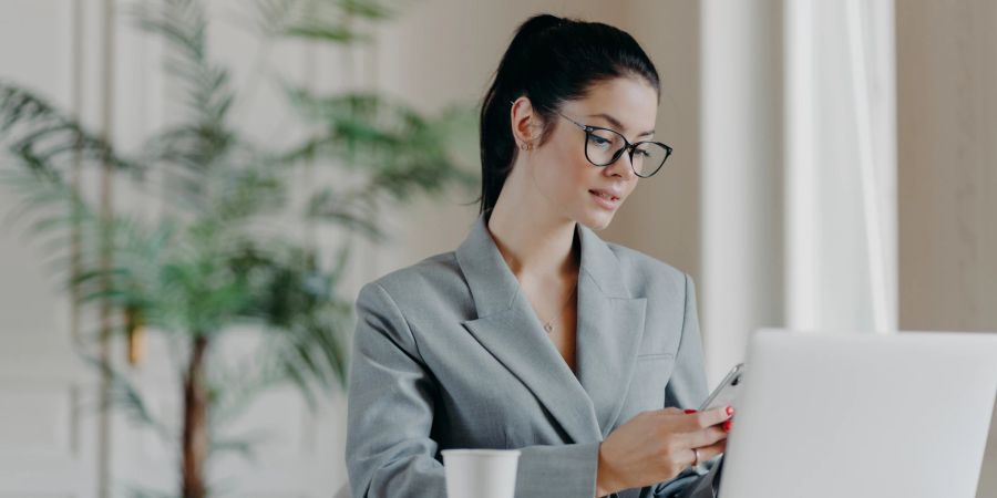 Junge Frau mit Laptop und Smartphone am Arbeitsplatz