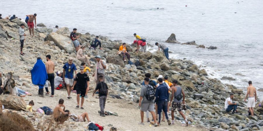 Menschen gehen am Strand entlang, während sie versuchen, von der marokkanischen Stadt Fnideq im Norden in die spanische Enklave Ceuta zu gelangen. Foto: STR/AP/dpa