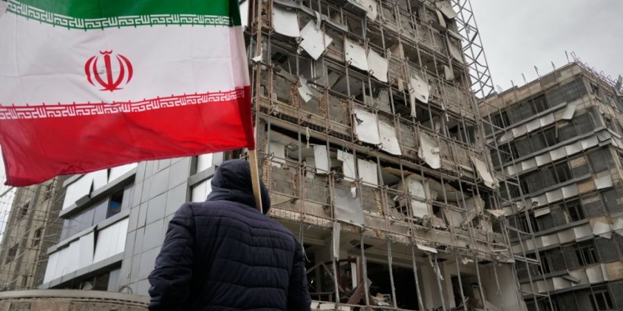 Ein Mann hält eine iranische Fahne neben dem beschädigten Gandhi-Krankenhaus, das am Sonntag während eines Angriffs auf einen Fernsehturm des staatlichen Fernsehens getroffen wurde. ...