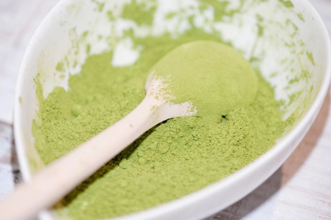 Grüntee – konkreter gesagt: Matcha – ist häufig Bestandteil von Detox-Pulvern. Diese werden zum Beispiel als Zutat für Smoothies verwendet. Matcha Grüntee Porzellan Löffel Holz
