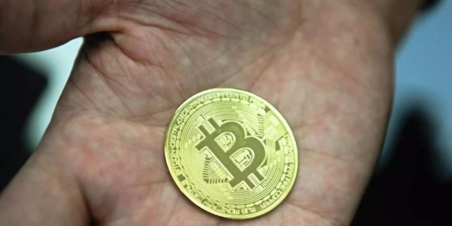 Ein Mann hält eine nachgemachte Münze mit dem Bitcoin-Logo in den Händen. Foto: Nicolas Armer/dpa