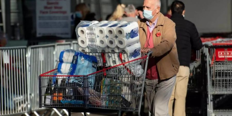 Ein Mann mit Maske schiebt einen Einkaufswagen voll mit Dosen, Getränken und Toilettenpapier in Birmingham an einem Costco-Markt vorbei. Foto: Jacob King/PA Wire/dpa