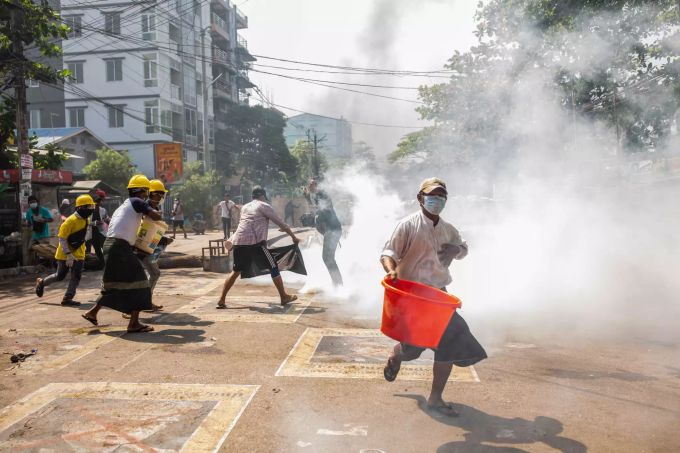 Gegner der Militärjunta von Myanmar laufen bei einem Protest gegen die Junta über die Strasse und kippen Wasser auf rauchende Tränengaskanister. Foto: Aung Kyaw Htet/SOPA Images via ZUMA Wire Nach dem Militärputsch in Myanmar