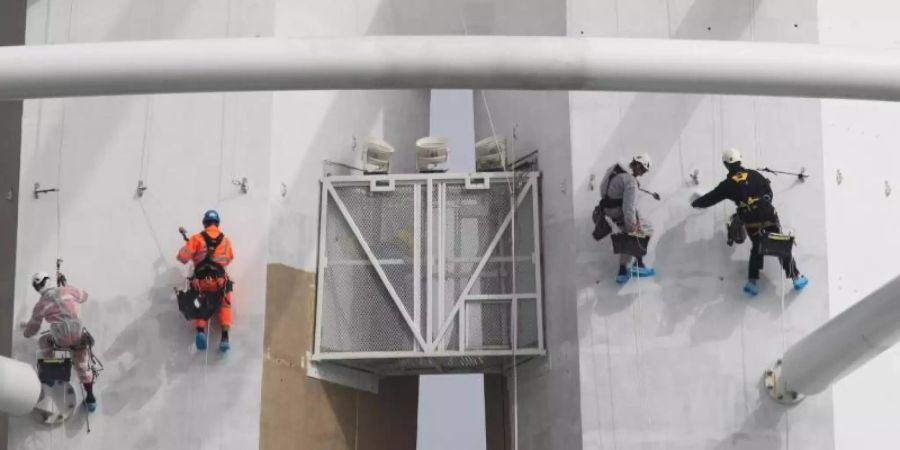 Spezialisten klettern an der Aussenseite des «Spinnaker Towers» und streichen dabei den Aussichtsturm im Hafen von Portsmouth. Foto: Andrew Matthews/PA Wire/dpa