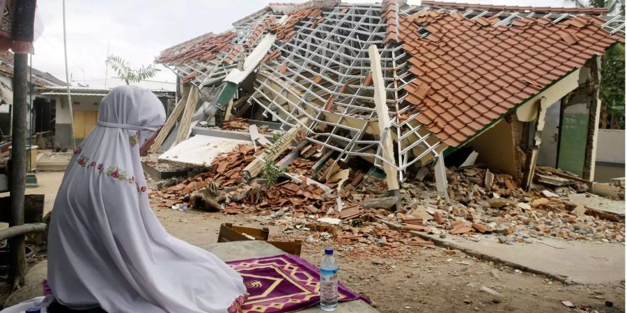 Eine Frau betet vor den Trümmern eines vom Erdbeben zerstörten Hauses auf der Insel Lombok.