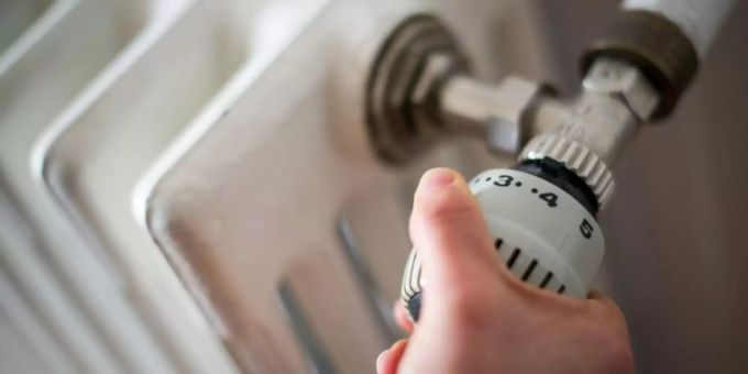 Eine Frau dreht am Thermostat einer Heizung. Heizen