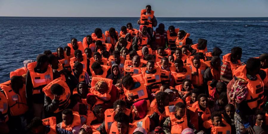 Mehrere Flüchtlinge aus verschiedenen afrikanischen Ländern sitzen vor der Küste von Libyen an Bord eines überfüllten Holzbootes und warten darauf, dass das spanische Rettungsschiff der Nichtregierungsorganisation Proactiva Open Arms sie rettet und nach Europa bringt.