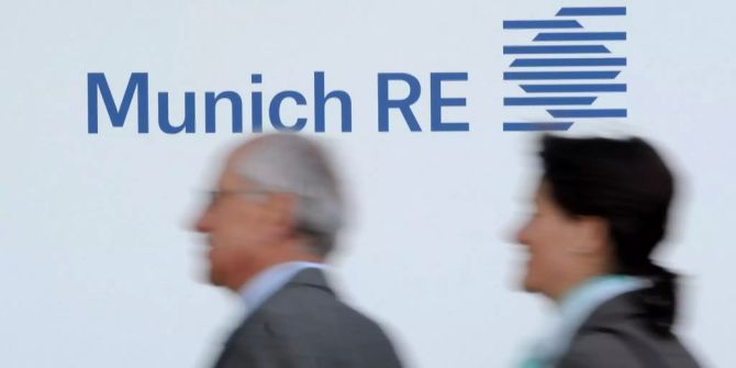 Zwei Personen laufen an dem Logo der Munich Re am Hauptsitz des Rückversicherers in München vorbei