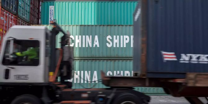 Ein Lastwagen fährt an chinesischen Containern vorbei.