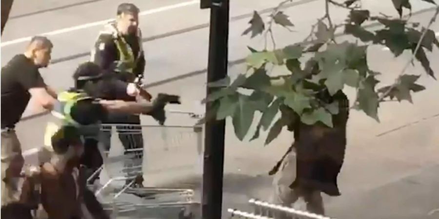 Das Standbild aus einem Video zeigt Michael Rogers (l, mit Einkaufswagen) und Polizisten, die einen Mann (r), der mit einem Messer bewaffnet ist, überwältigen zu versuchen.