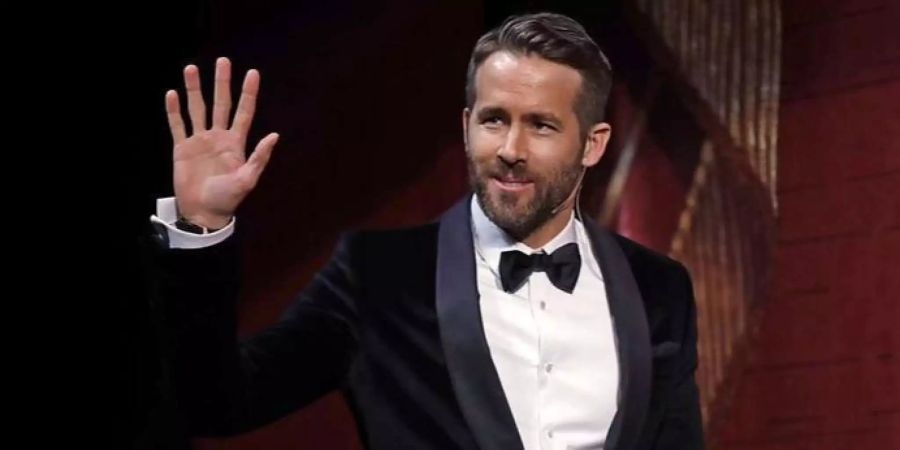 Ryan Reynolds winkt und hat dabei ein verschmitztes Lächeln auf.