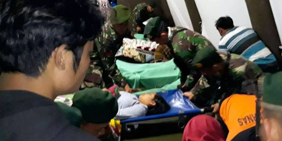 Indonesische Soldaten tragen eine verletzte Frau in ein Zelt.