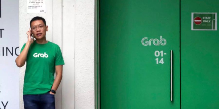 Ein Mann mit einem T-Shirt von Grab telefoniert neben dem Personaleingang einer Filiale des südostasiatischen Mitfahrdienstes  in Singapur.