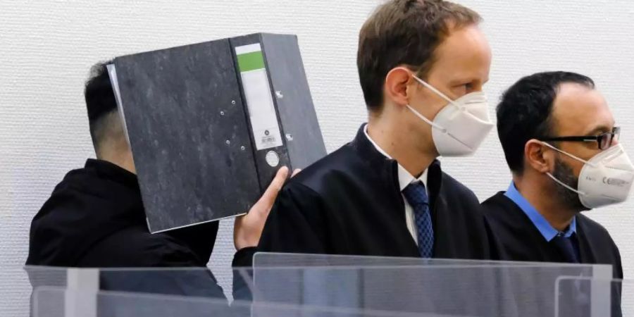 Der Angeklagte verbirgt im Sitzungssaal des Landgerichts Ingolstadt sein Gesicht hinter einem Aktenordner. Davor stehen seine Verteidiger. Foto: Ulf Vogler/dpa/Archiv
