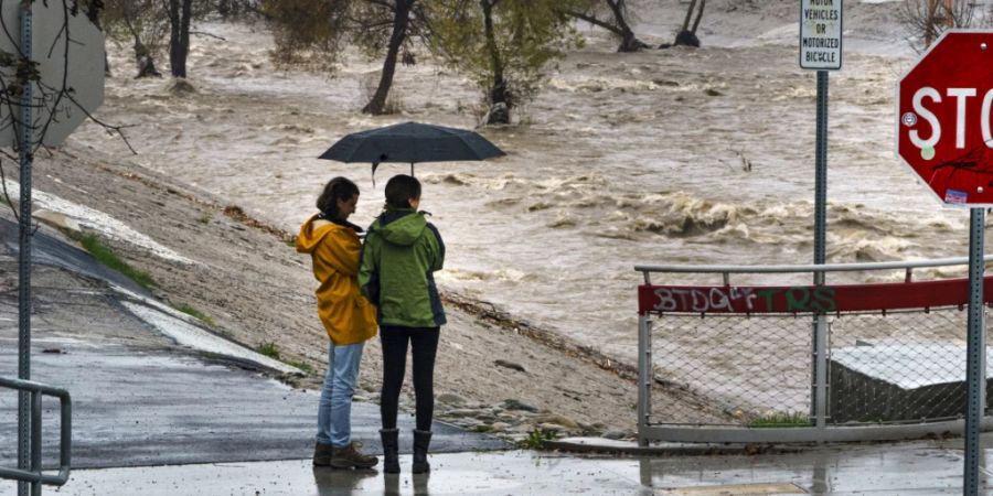 Menschen beobachten die grossen Mengen an Regenwasser im Los Angeles River. Nach den schweren Tornados mit mindestens neun Todesopfern im Südosten der USA gehen die Suche nach möglichen weiteren Opfern sowie die Aufräumarbeiten weiter. Foto: Damian Dovarganes/AP/dpa