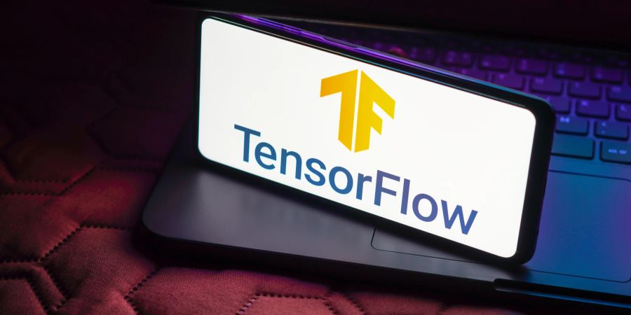 Auf einem Laptop steht ein Smartphone auf dessen Bildschirm das Logo von TensorFlow gezeigt wird.