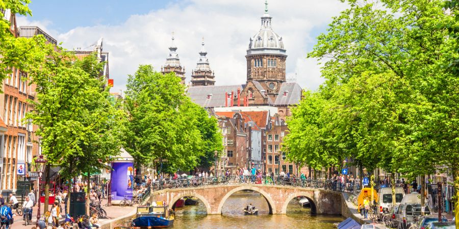 Touristen auf einem Kanal in Amsterdam mit Brücke im Hintergrund.