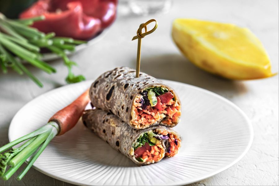 Tortilla mit Mango-Karottensprossen und Hummus und Karotte auf einem Teller.