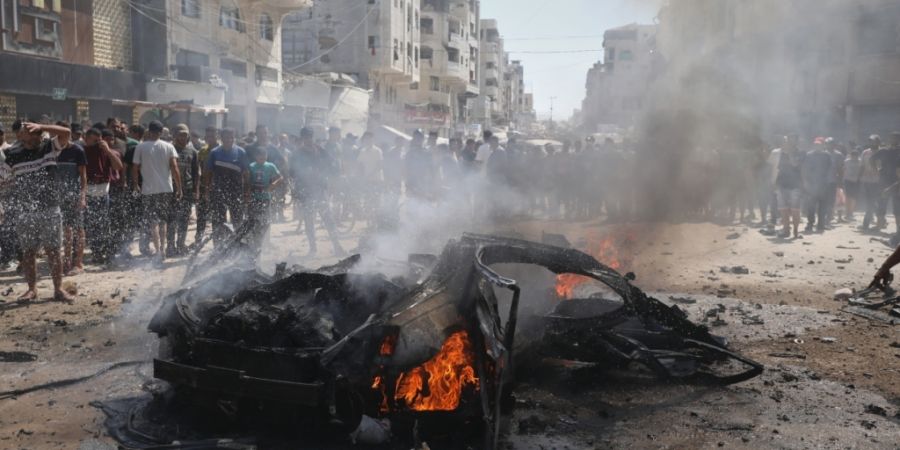 Palästinenser versammeln sich nach einem israelischen Angriff in Stadt Gaza um das Wrack eines Autos. Foto: Yousef Alzanoun/AP/dpa