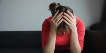 Verzweifelte Frau mit gesenktem Kopf und Händen am Kopf