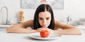 Frau starrt Tomate auf einem Teller an. Hungern, Diät.