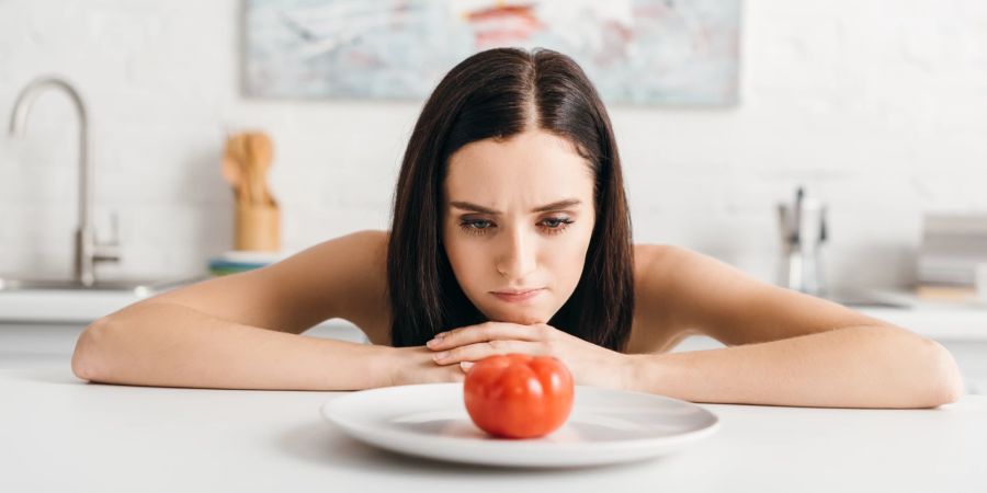 Frau starrt Tomate auf einem Teller an. Hungern, Diät.