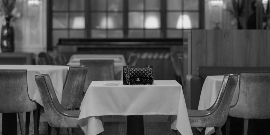 Hier zu sehen: die Chanel-Tasche auf dem Tisch, an dem die beiden Charaktere Platz nehmen.