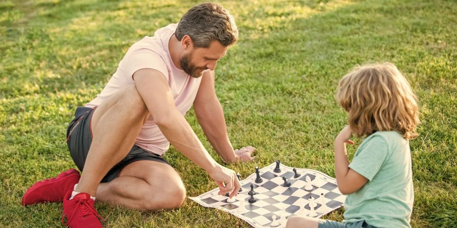 Ein Vater und sein Sohn spielen Schach im Park.