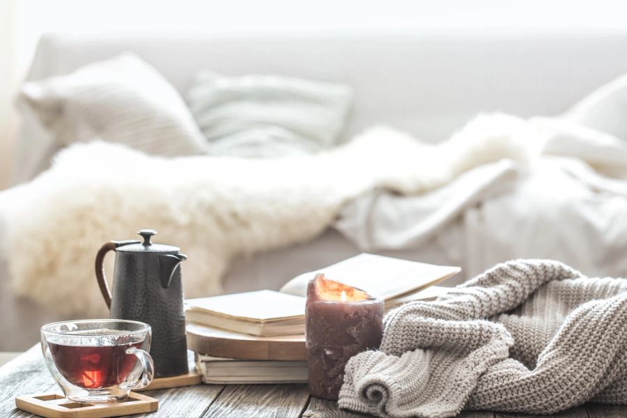 Ein Interieur mit weichen Decken, flauschigen Kissen, einer Tasse Tee und einer Kerze auf dem Tisch.