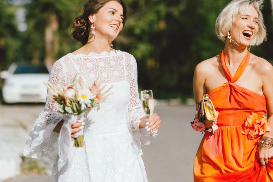 Die glückliche Braut und ein Gast in orangem Kleid.