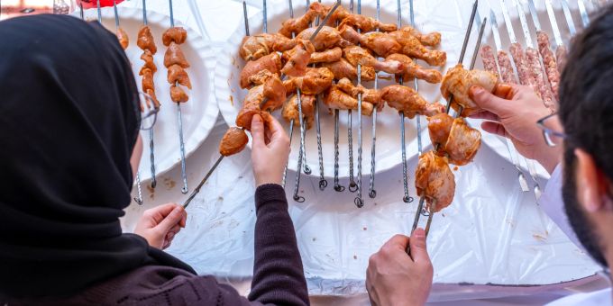 Ein Highlight der libanesischen Küche in Beirut sind die aromatischen Kafta-Hühnchenspieße, die mit einer einzigartigen Mischung aus Gewürzen, frischen Kräutern und oft auf Holzkohle gegrillt serviert werden – ein wahres Geschmackserlebnis! Hühnchenspiesse auf dem Grill, Frau mit Kopftuch